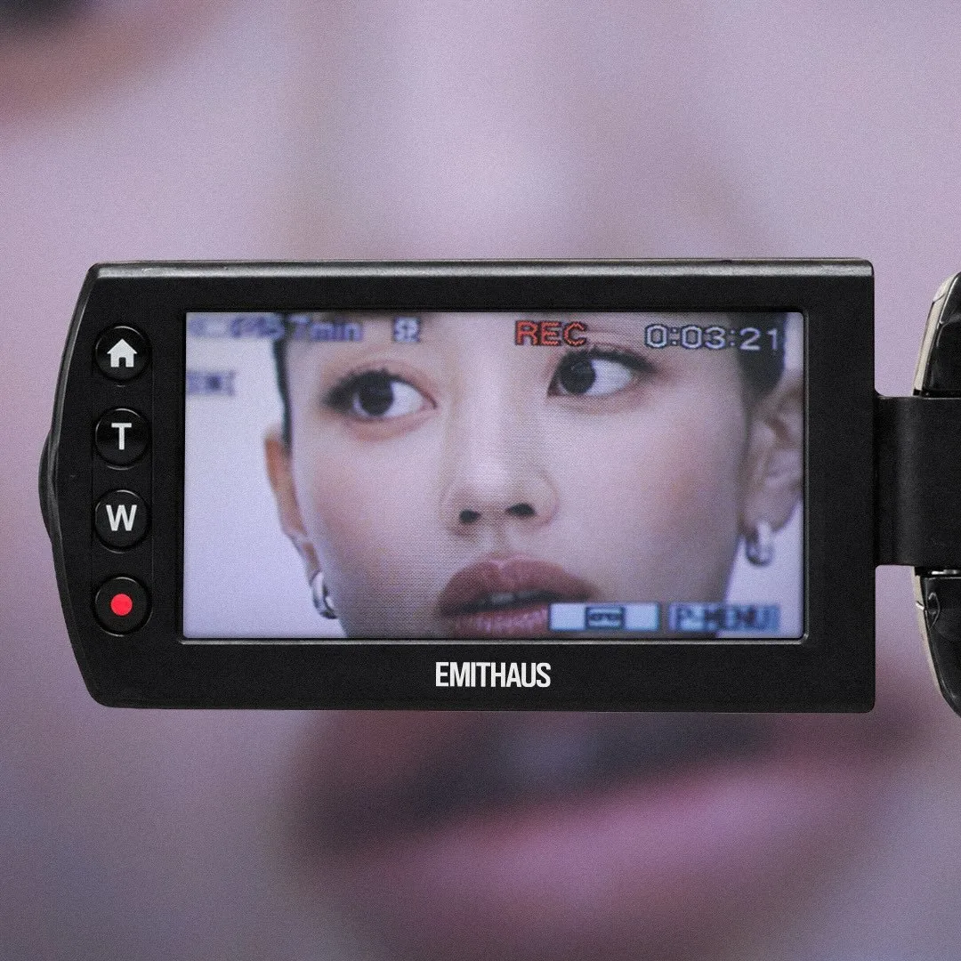 A camcorder screen showing a close-up of Jihyo recording, with the EMITHAUS wordmark below