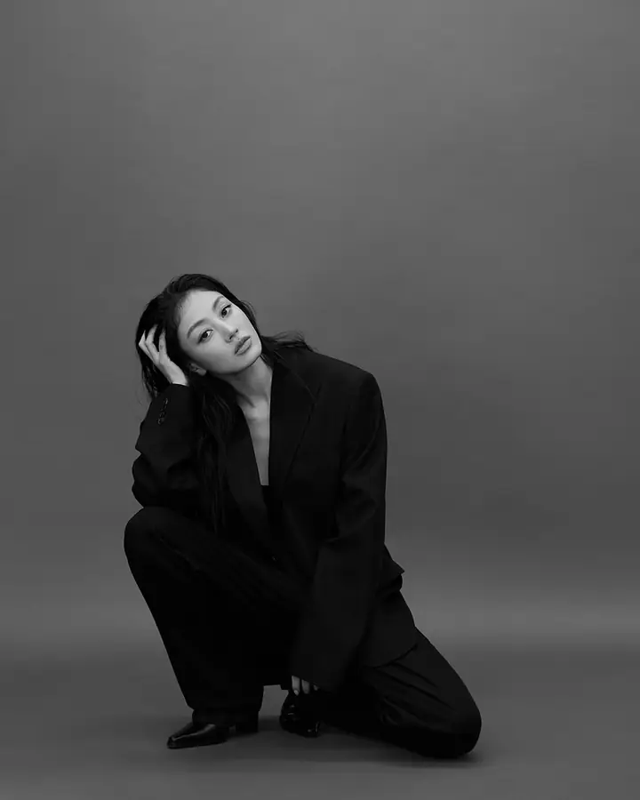 Jihyo crouching in a black suit against a grey backdrop